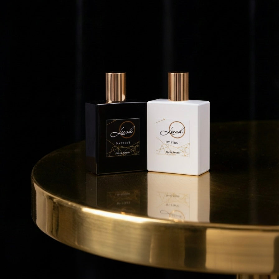 Two perfume bottles, one black and one white, on a reflective gold surface with a dark background. Her first and his first perfume bottles by leesh fragarnces, displayed together in a cinematic editorial style, luxury fragrances for day and special occasions