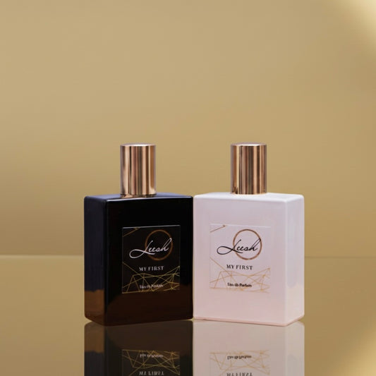 Two perfume bottles, one black and one white, with 'Leesh' branding on a beige background. - His and Her My First fragrances by Leesh — Her My First features patchouli, cedarwood, vanilla, jasmine, rose, ylang-ylang, amber, and musk. His My First features cedarwood, amber, bergamot, and black pepper. Celebrate unforgettable first moments with these bold, confident, and empowering scents.
